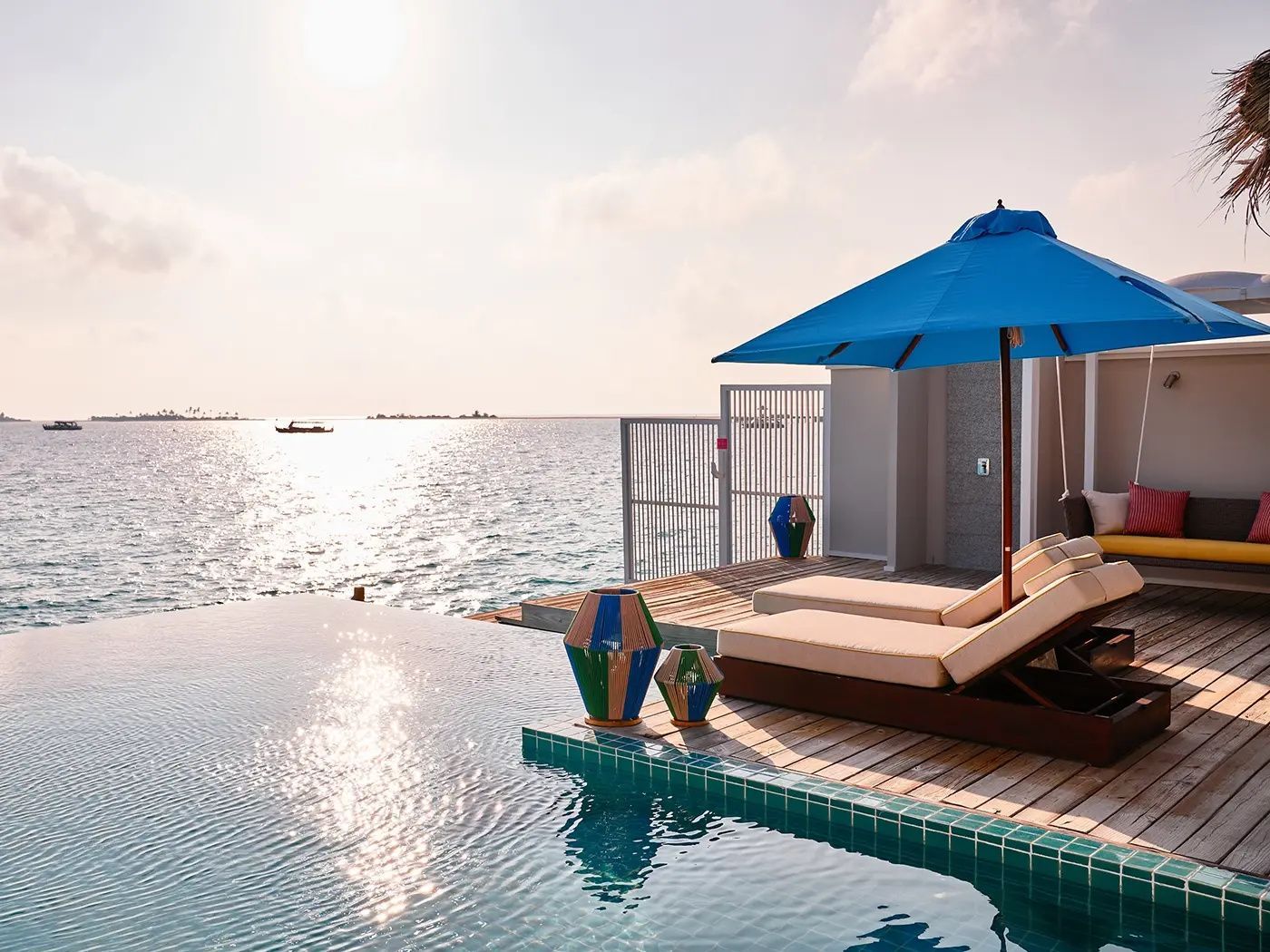 Sonnendeck einer Overwater-Villa mit Pool, Sonnenliegen und Blick auf das Meer.