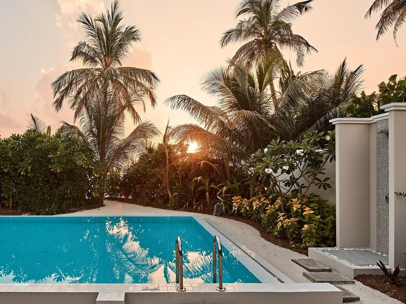 Türkisfarbener Pool einer Villa bei Sonnenuntergang umgeben von Palmen.