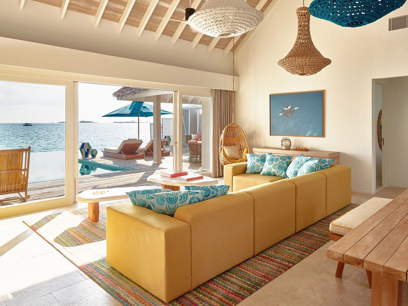 Helles Wohnzimmer einer Villa mit gelbem Sofa und Blick auf die Terrasse mit Pool.