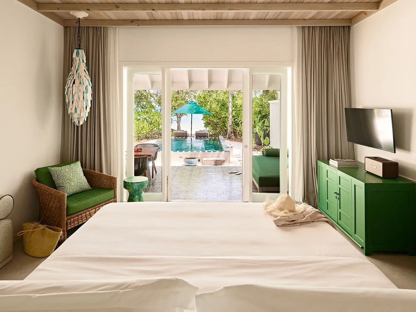 Helles Schlafzimmer mit Doppelbett und Blick auf Terrasse, Pool und Palmen.