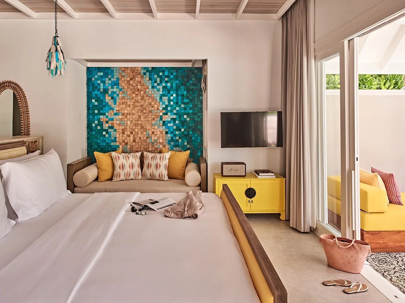Schlafbereich mit Bett, Tagesbett vor blau-goldenem Mosaik und gelber Kommode.