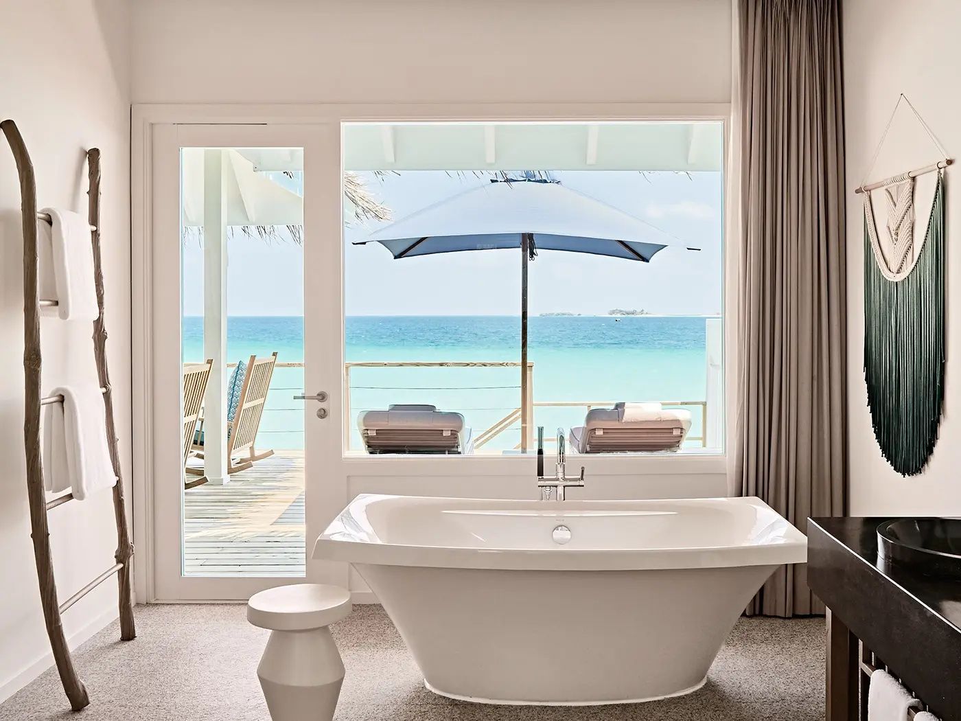 Freistehende weiße Badewanne vor großem Fenster mit Blick auf das Meer.