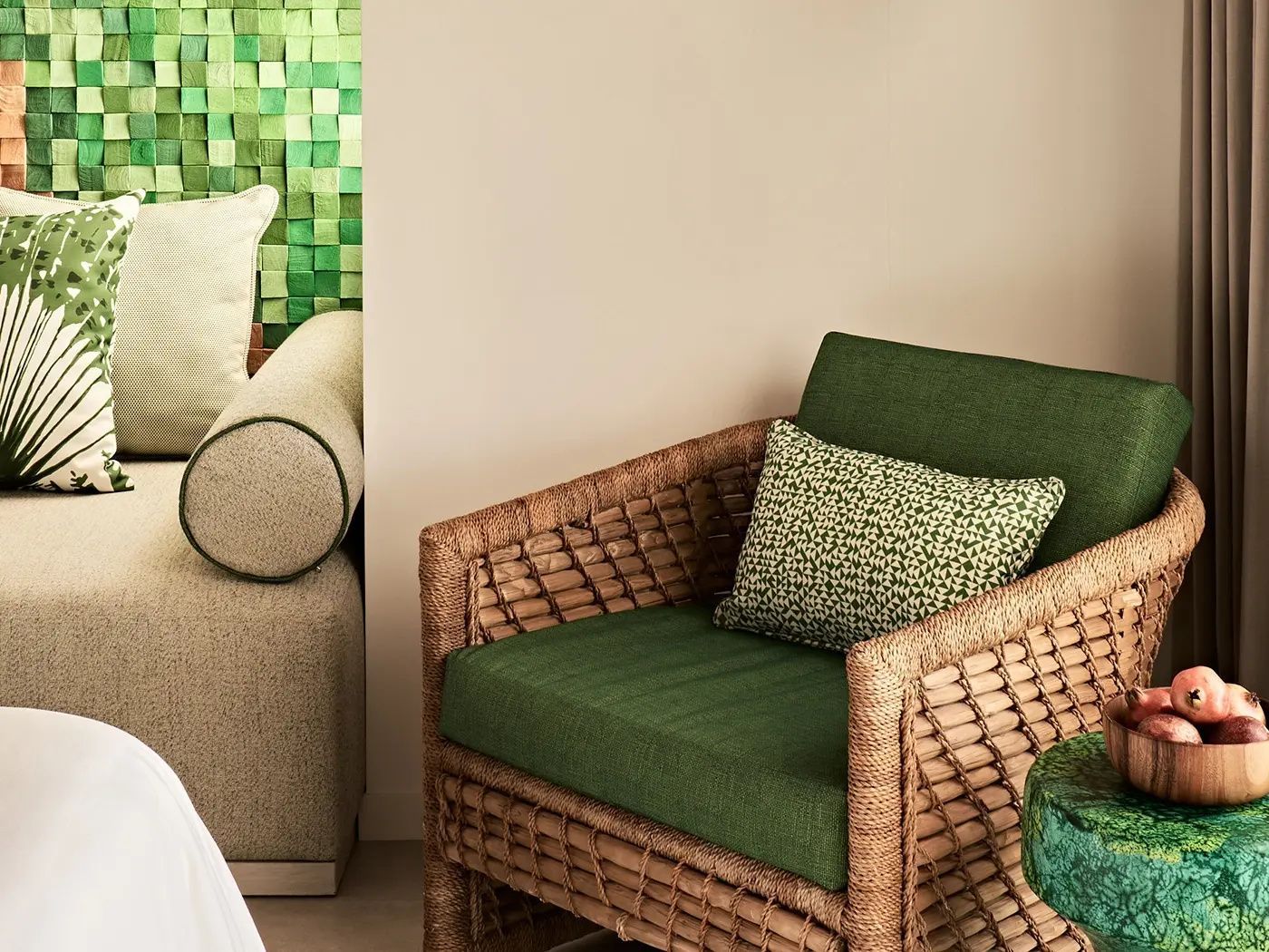 Sessel aus Geflecht mit grünem Kissen neben einer grünen Mosaikwand.