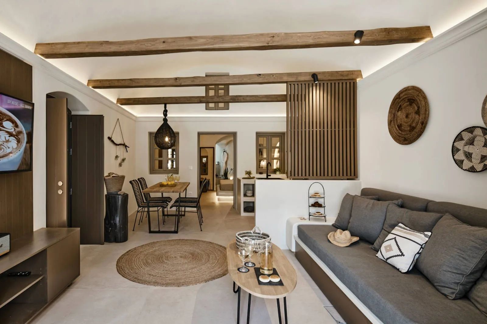 Wohnbereich mit grauem Sofa, großem Teppich, Holzbalken an der Decke und Essplatz.