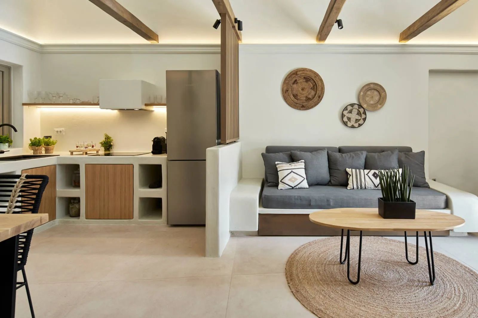 Wohnbereich einer Suite mit grauer Couch, Holztisch und kompakter Küchenzeile.