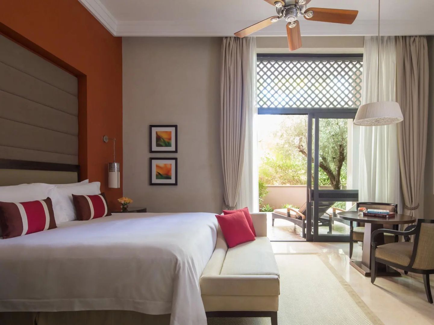 Modernes Hotelzimmer mit großem Doppelbett, roter Wand und Zugang zur eigenen Terrasse mit Liegestuhl.