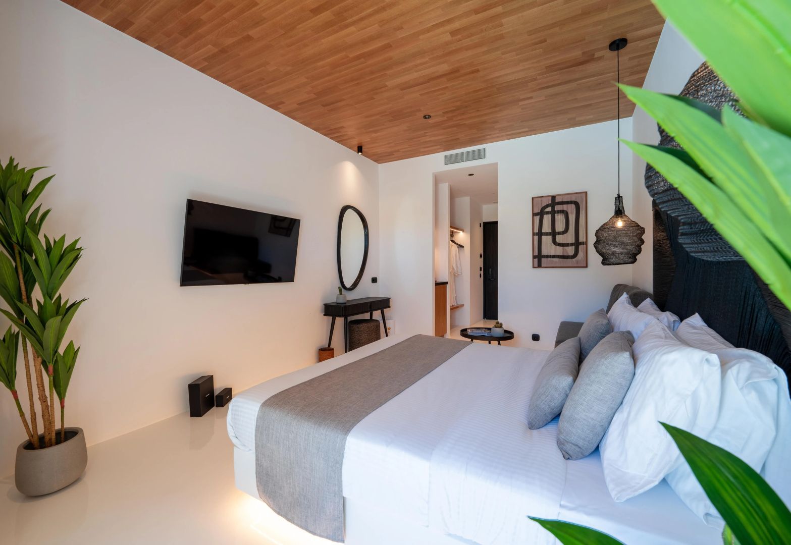 Hell eingerichtetes Schlafzimmer mit Holzdecke, Wand-TV, Spiegel und Schminktisch.