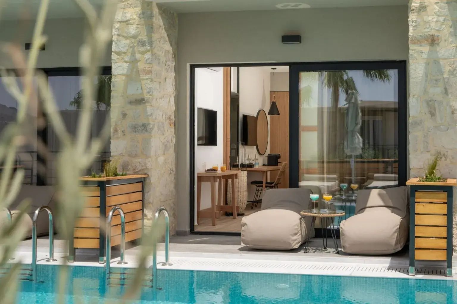 Liegebereich am Pool mit gemütlichen Sitzkissen und Glasfront zur Suite.