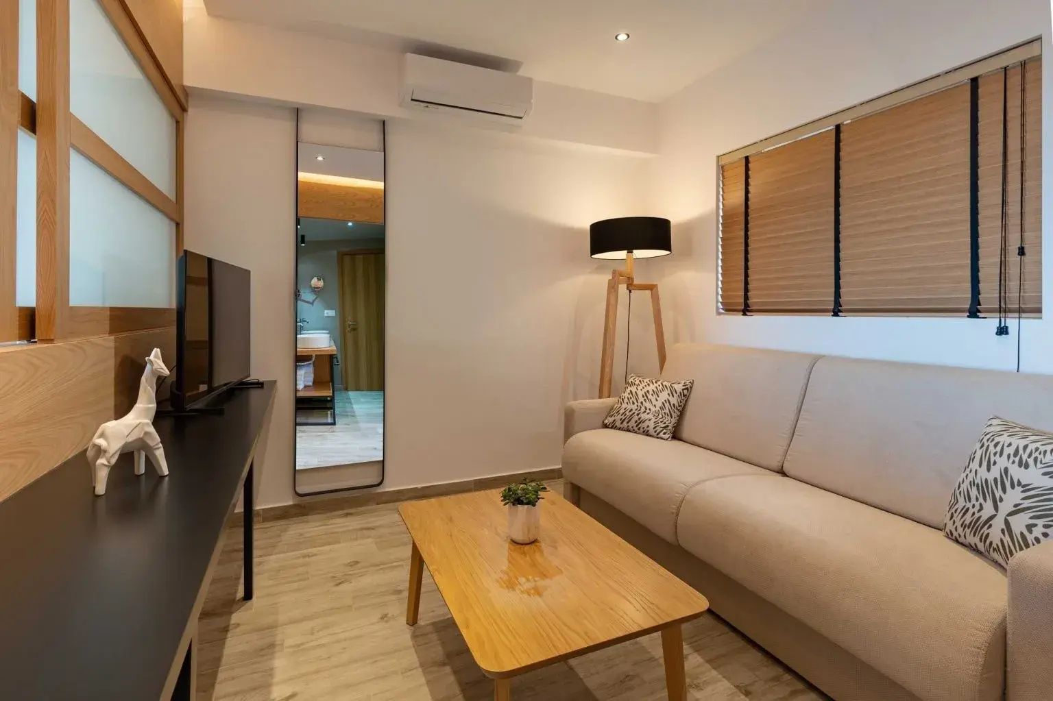 Modern eingerichteter Wohnbereich mit beige verkleidetem Sofa, Holzcouchtisch und Stehleuchte.