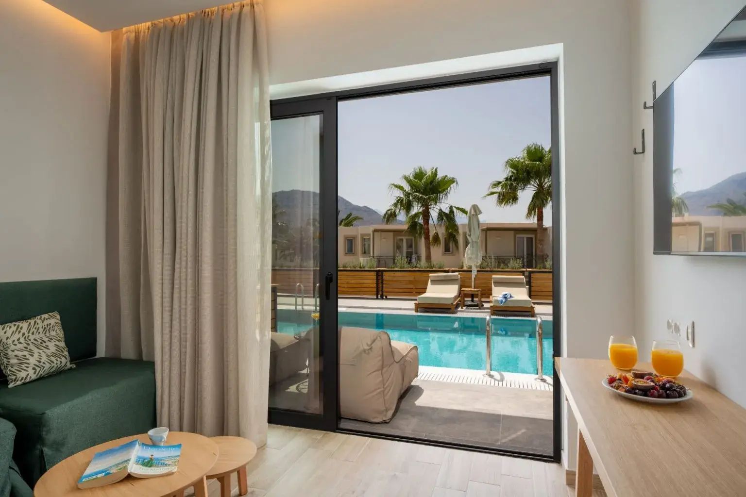 Blick durch die Glastür auf die Terrasse mit Sonnenliegen und Swim-up-Pool.
