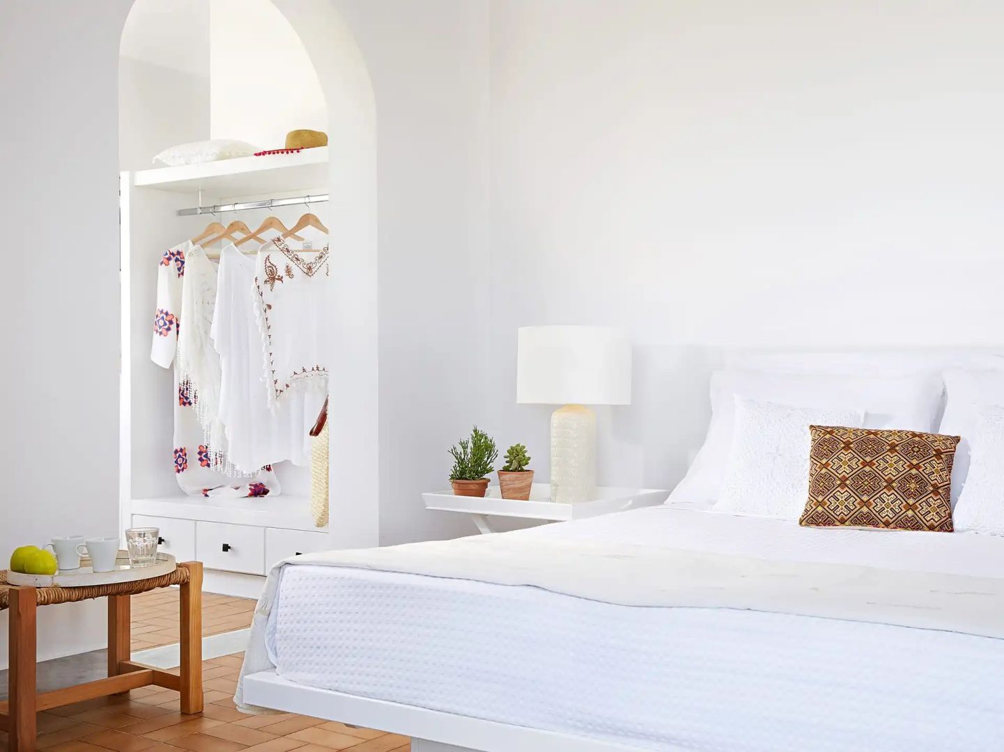 Hell eingerichtetes Schlafzimmer mit weißen Möbeln und Bett sowie einer Kleidernische.
