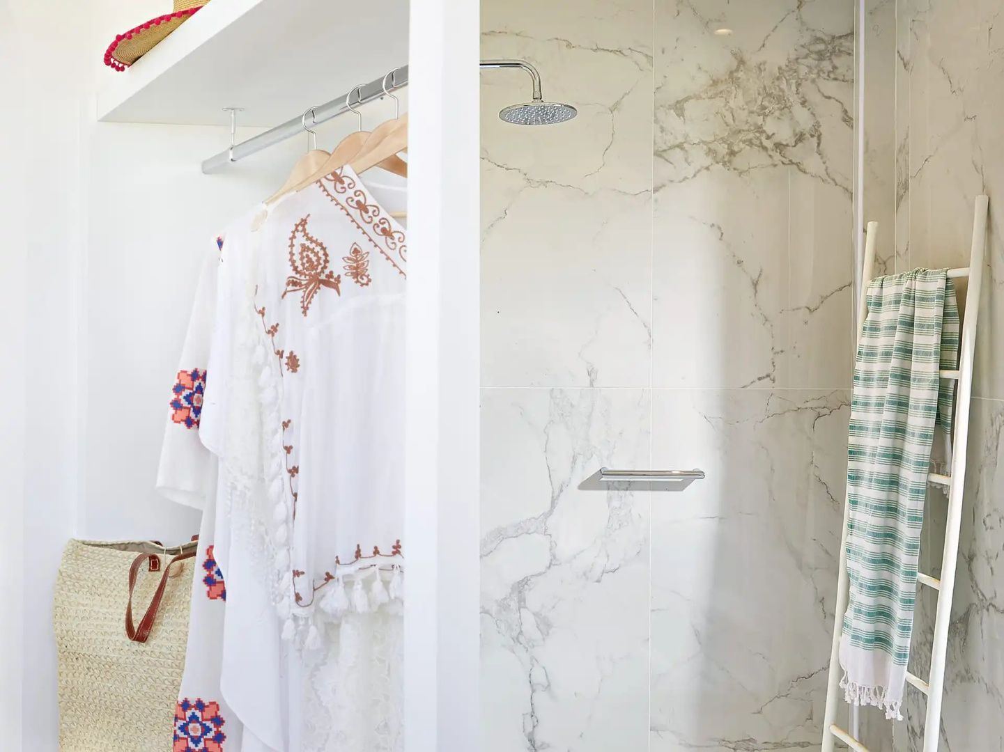 Blick in die Dusche mit Marmorwand und Regenduschkopf neben einer Kleiderstange.