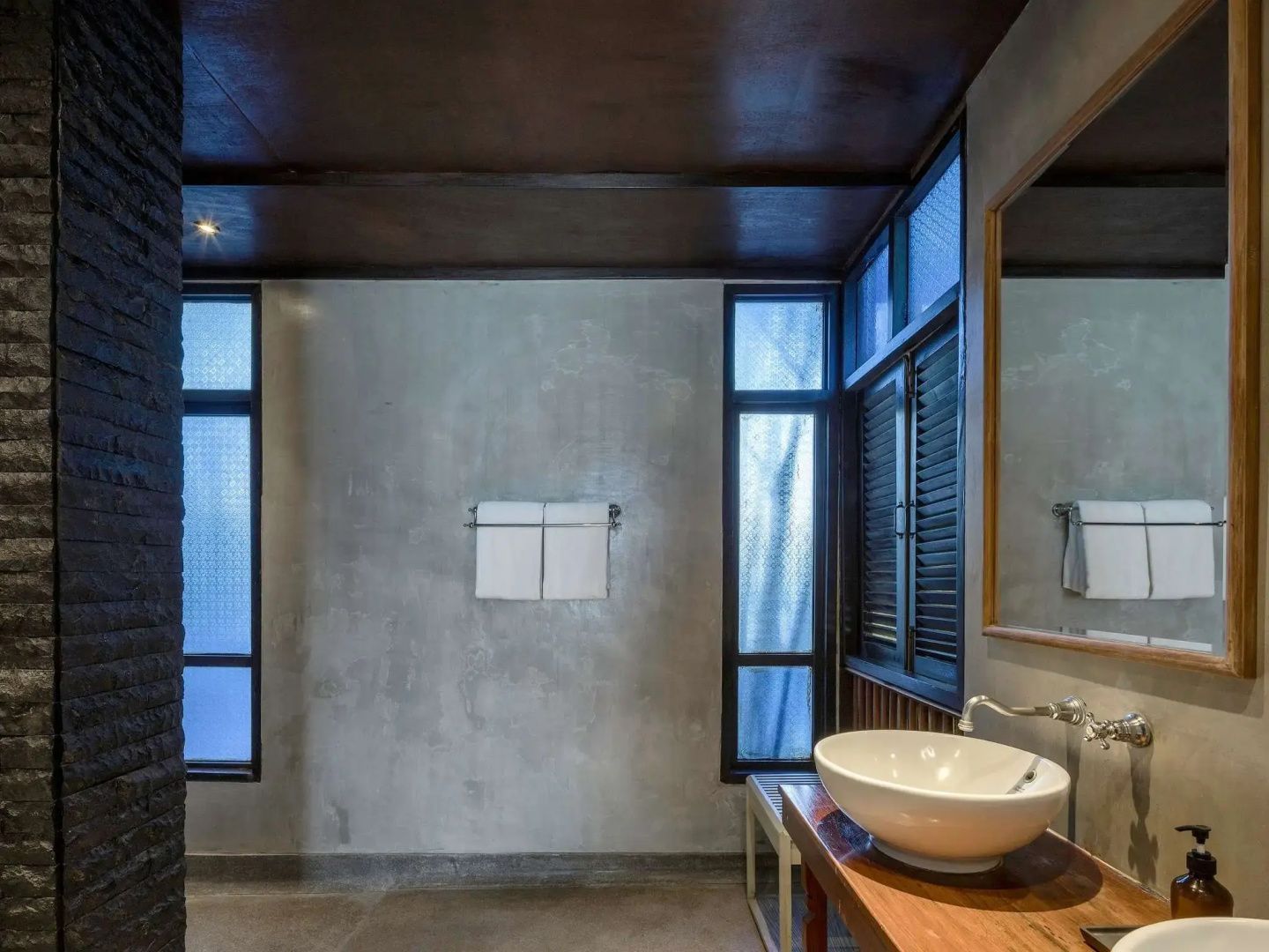 Modernes Badezimmer mit weißem Aufsatzwaschbecken auf Holztisch und Sichtbetonwand.