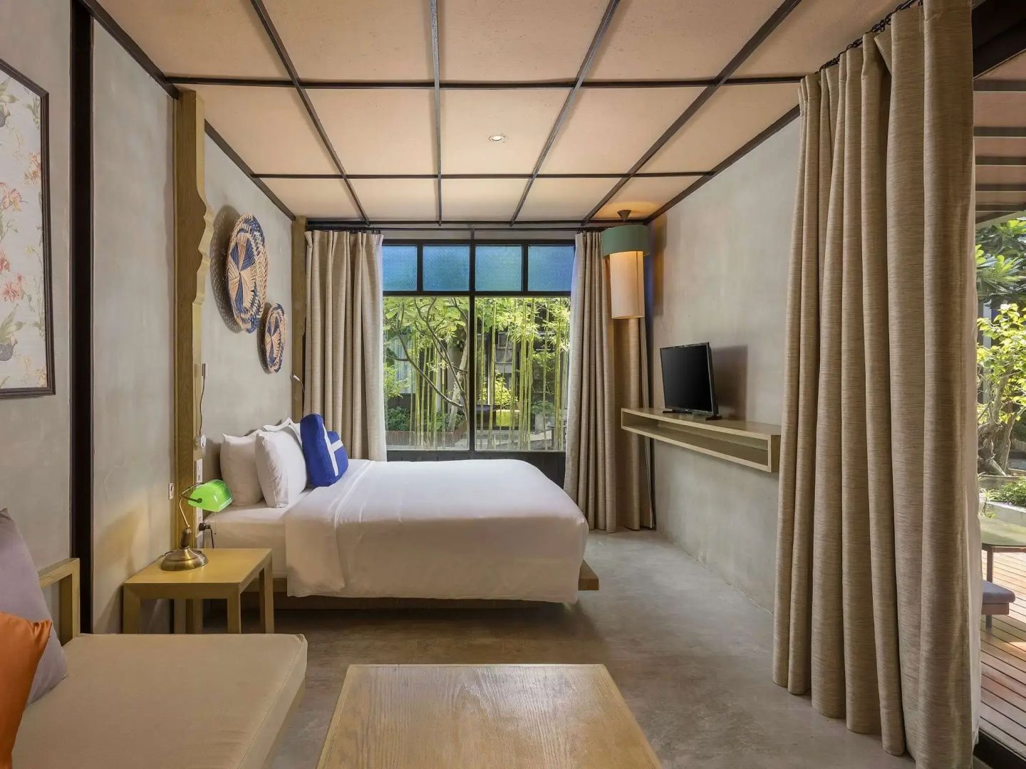 Doppelbett in modernem Hotelzimmer mit Holzdecke, Fernseher und Blick in den Garten.
