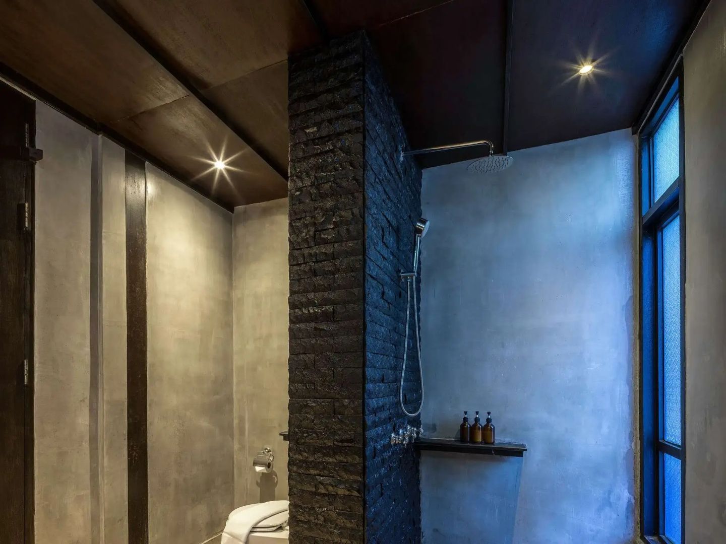 Badezimmerbereich mit dunkler Klinkerwand, Regendusche und separat integrierter Toilette.