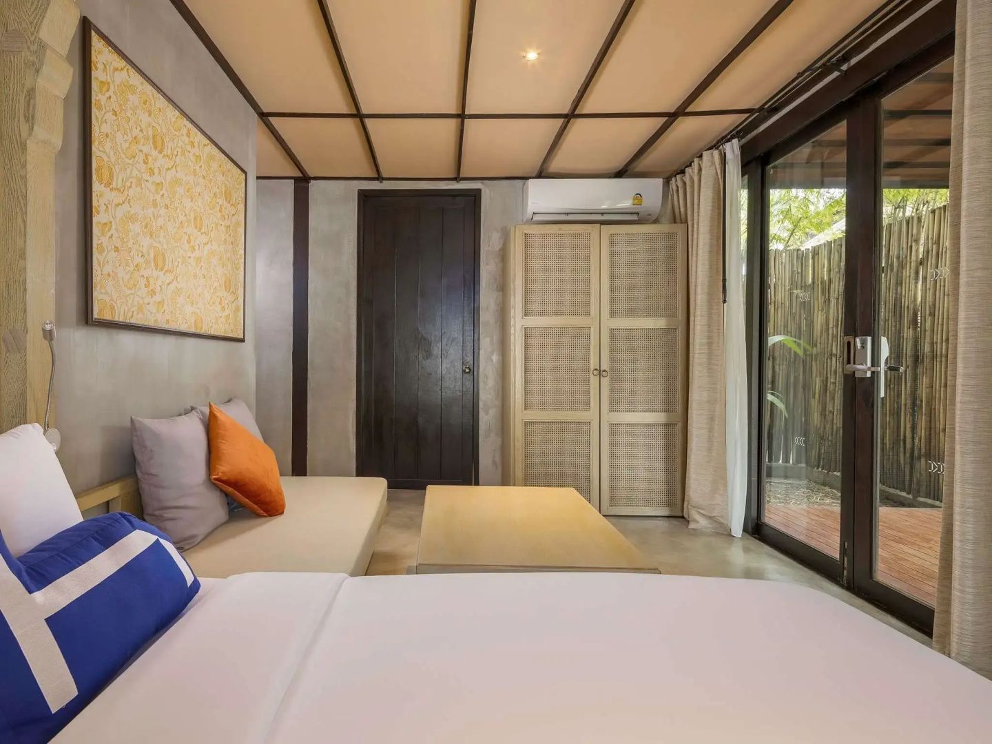 Sitzbereich im Hotelzimmer mit Sofa, Holztisch, Schrank aus Geflecht und Glas-Schiebetür.