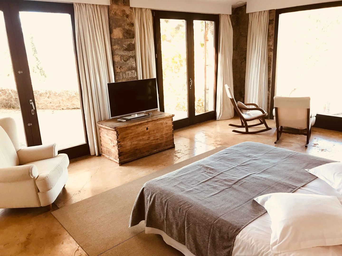 Helles Hotelzimmer mit Doppelbett, Fernseher auf Holzkiste und Schaukelstuhl.