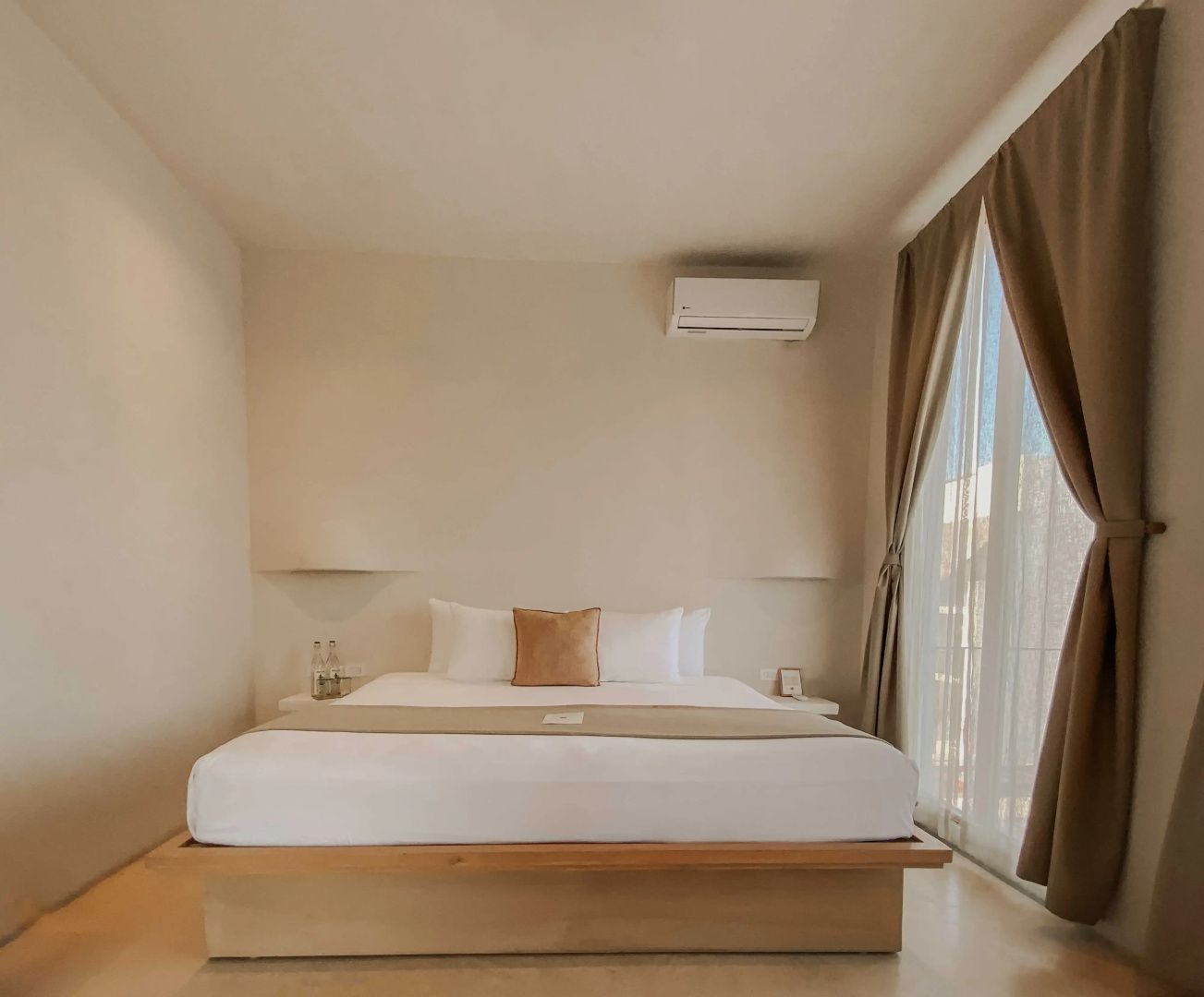 Helles Hotelzimmer mit einem großen Holzdoppelbett und einer Klimaanlage an der Wand.