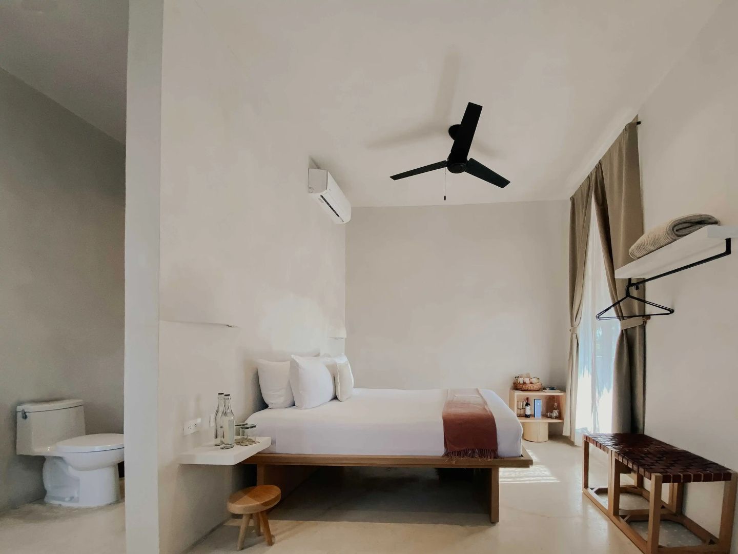 Hotelzimmer mit weißem Doppelbett, schwarzem Deckenventilator und bodentiefen Vorhängen.