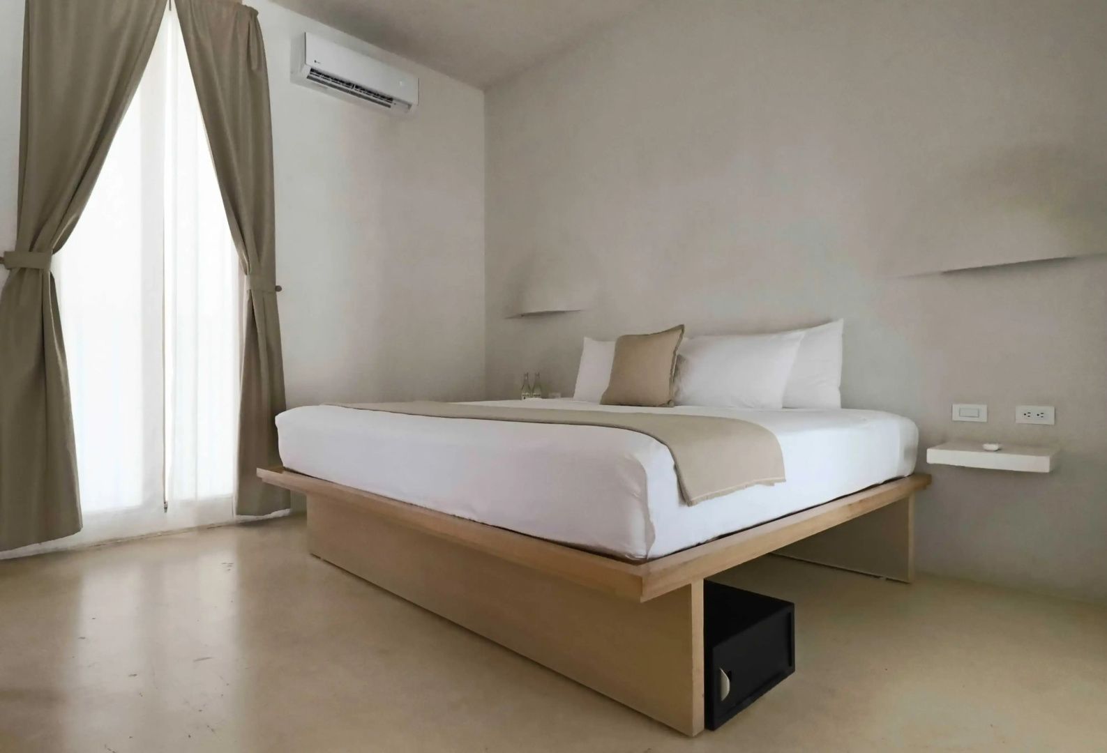 Holzdoppelbett in einem hellen Hotelzimmer mit beigefarbenen Vorhängen und Wandklimaanlage.