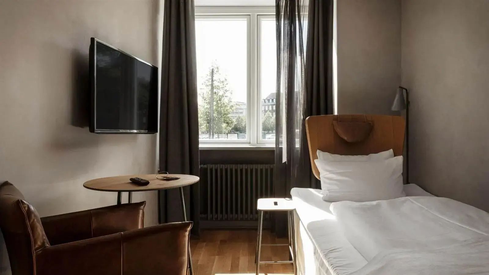 Ein eingerichtetes Hotelzimmer mit Holzboden, Fernseher, Tisch und hellem Bett.