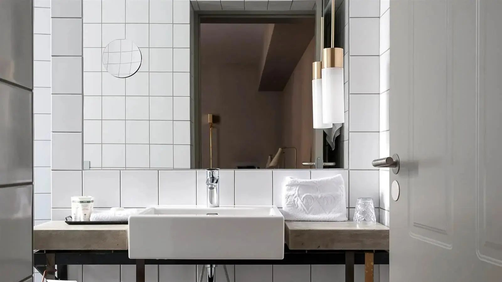 Badezimmer mit weiß gefliesten Wänden, modernem Waschtisch und Hängelampen.