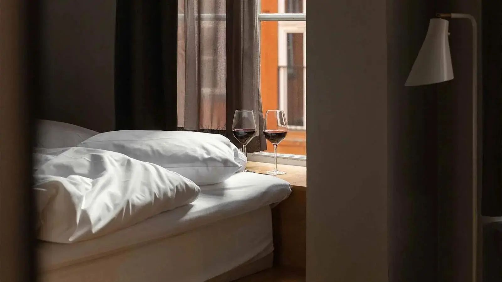 Zwei gefüllte Rotweingläser stehen auf einem Holzfensterbrett neben einem Bett.