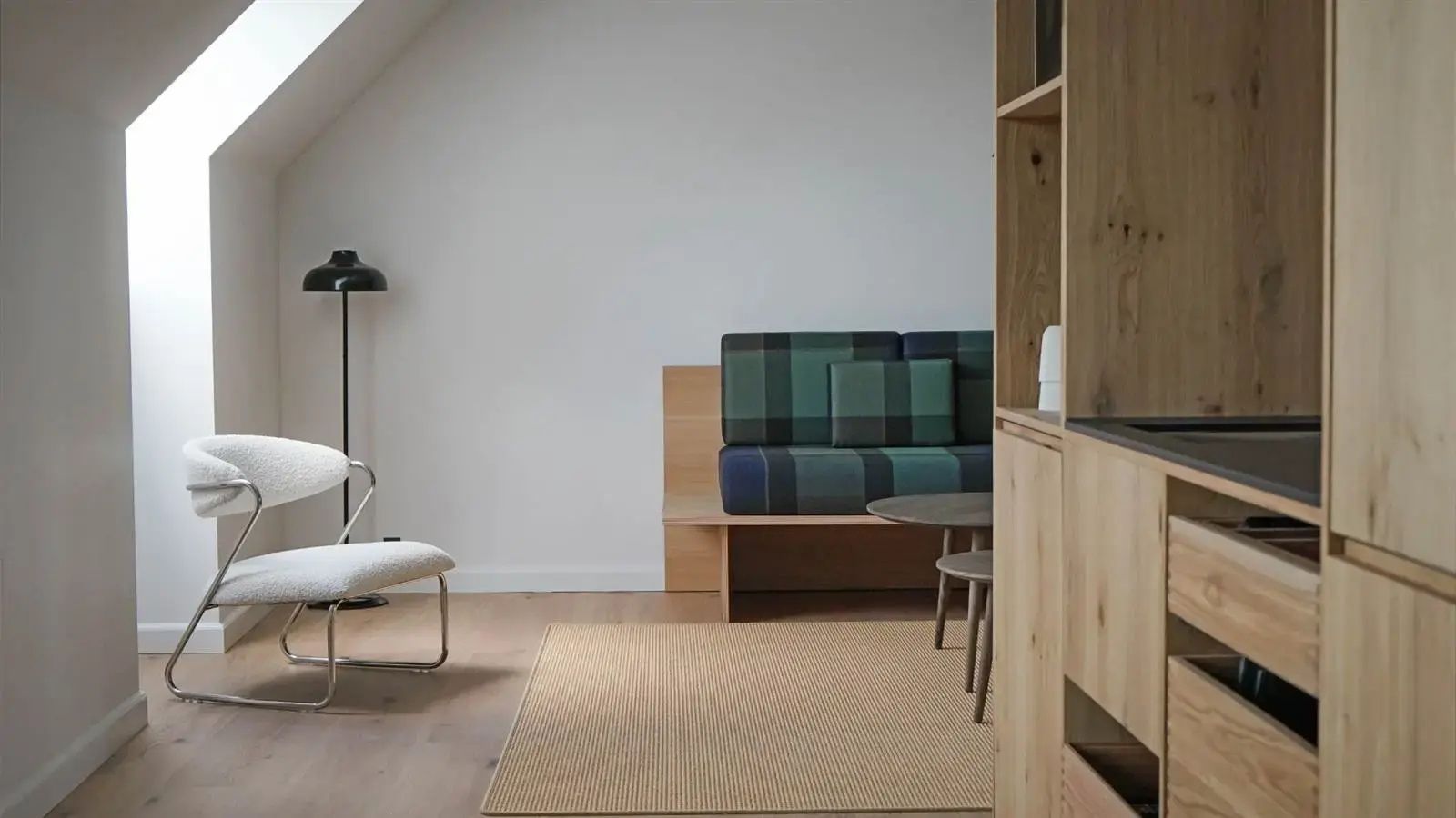 Sitzbereich unter einer Dachschräge mit kariertem Sofa, Holzregal und hellem Teppich.