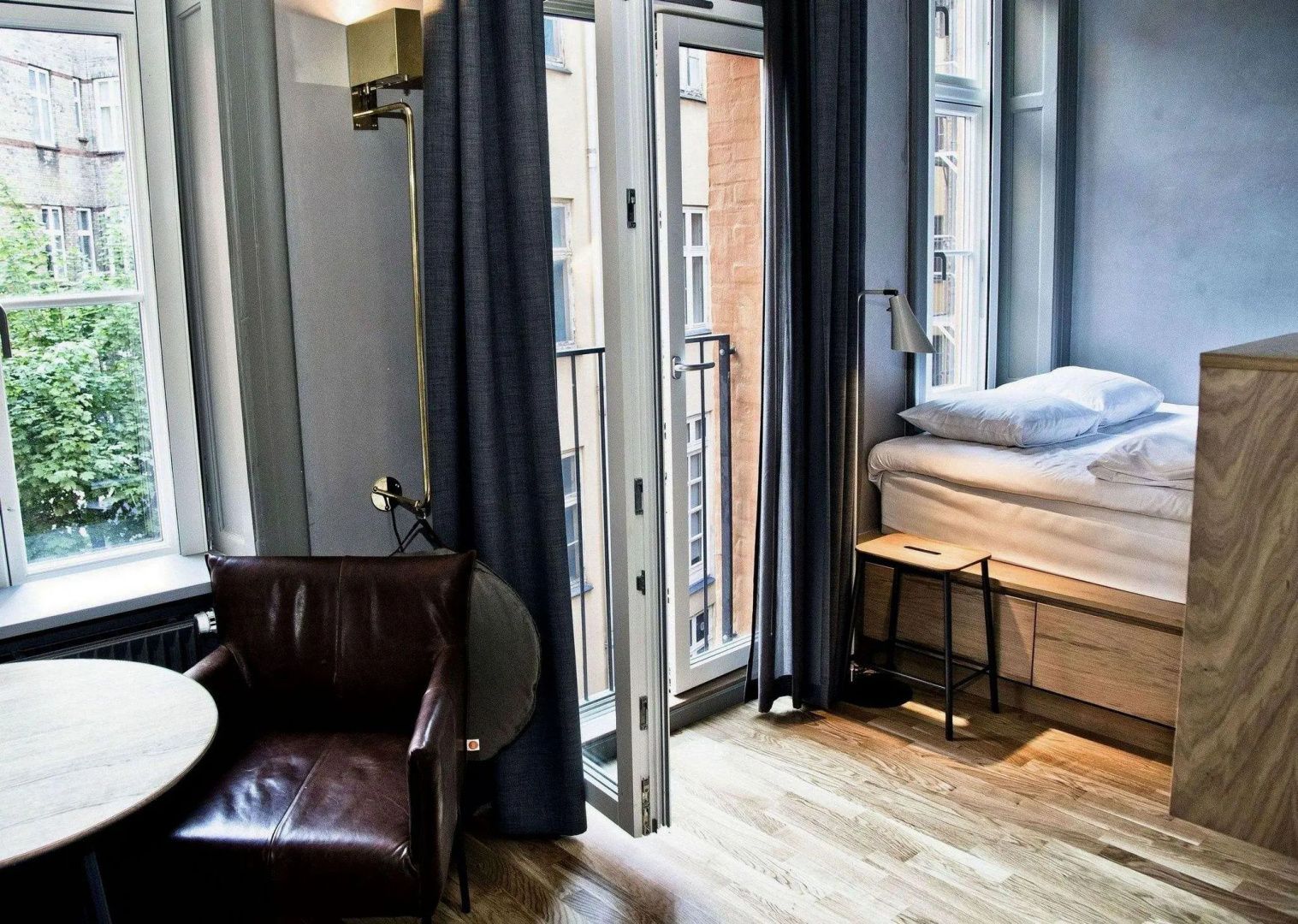 Hotelzimmer mit braunem Ledersessel, Parkettboden und Tür zum Balkon.