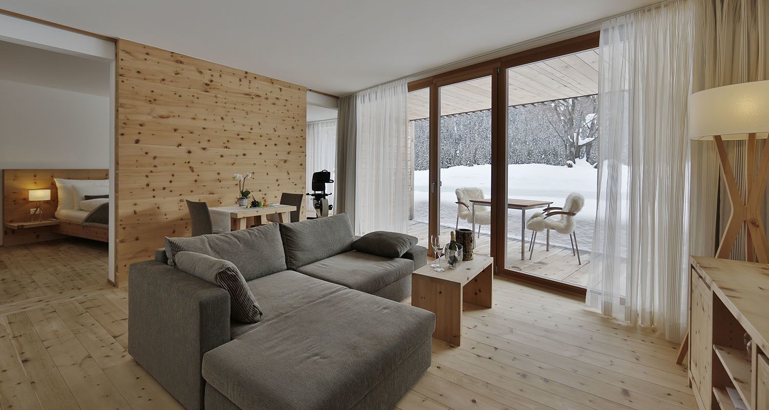 Wohnbereich mit Arvenholzwand, grauem Sofa und Blick auf die verschneite Terrasse.