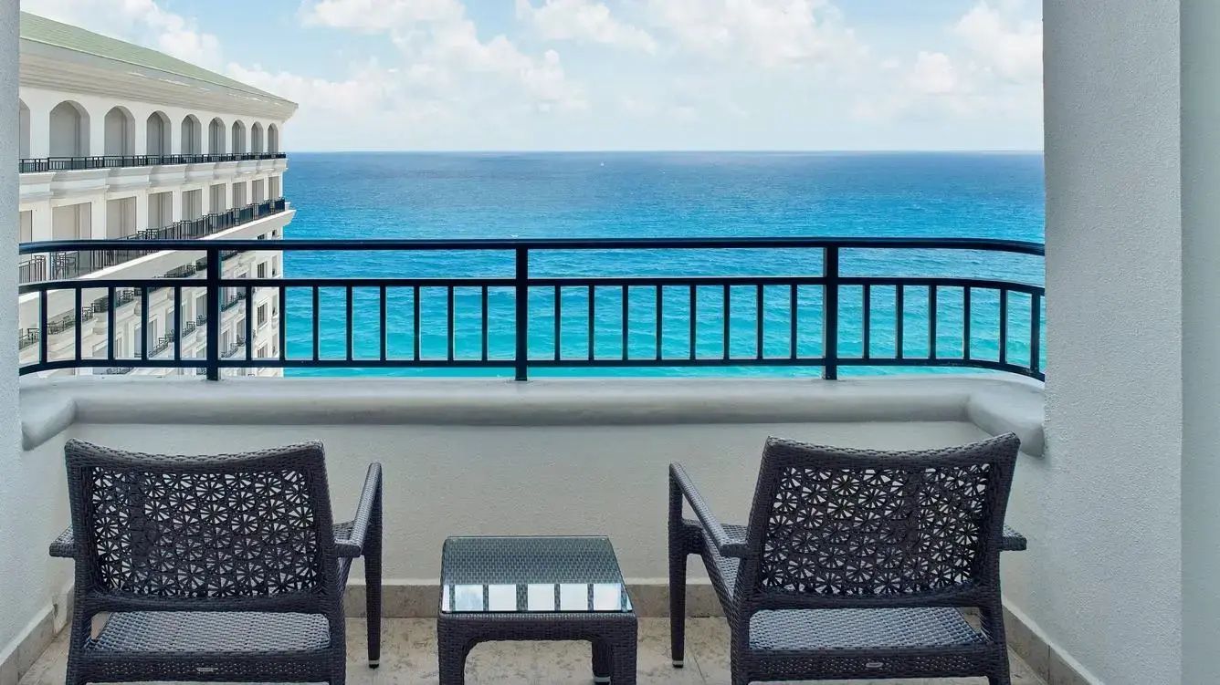 Zwei dunkle Stühle und ein Beistelltisch auf einem Balkon mit Blick auf das blaue Meer.