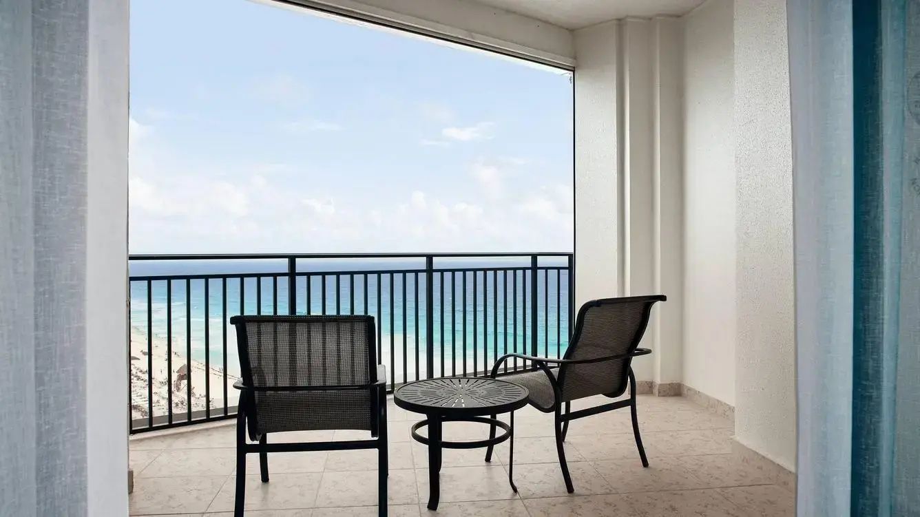 Balkon mit zwei schwarzen Stühlen und einem Tisch mit Blick auf das blaue Meer.