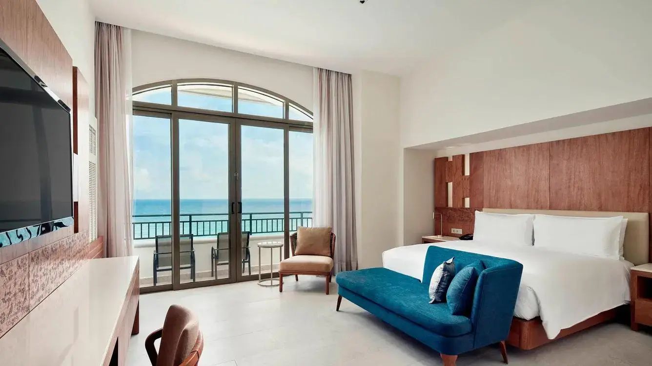 Hotelzimmer mit Doppelbett, blauem Sofa und Balkontür mit Blick auf das Meer.
