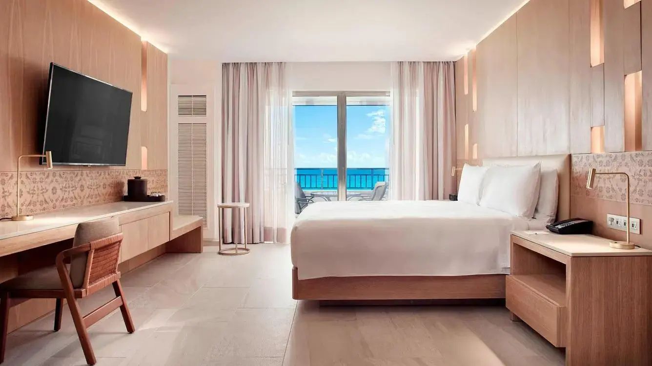 Helles Hotelzimmer mit Doppelbett und Blick durch die Balkontür auf das türkisfarbene Meer.