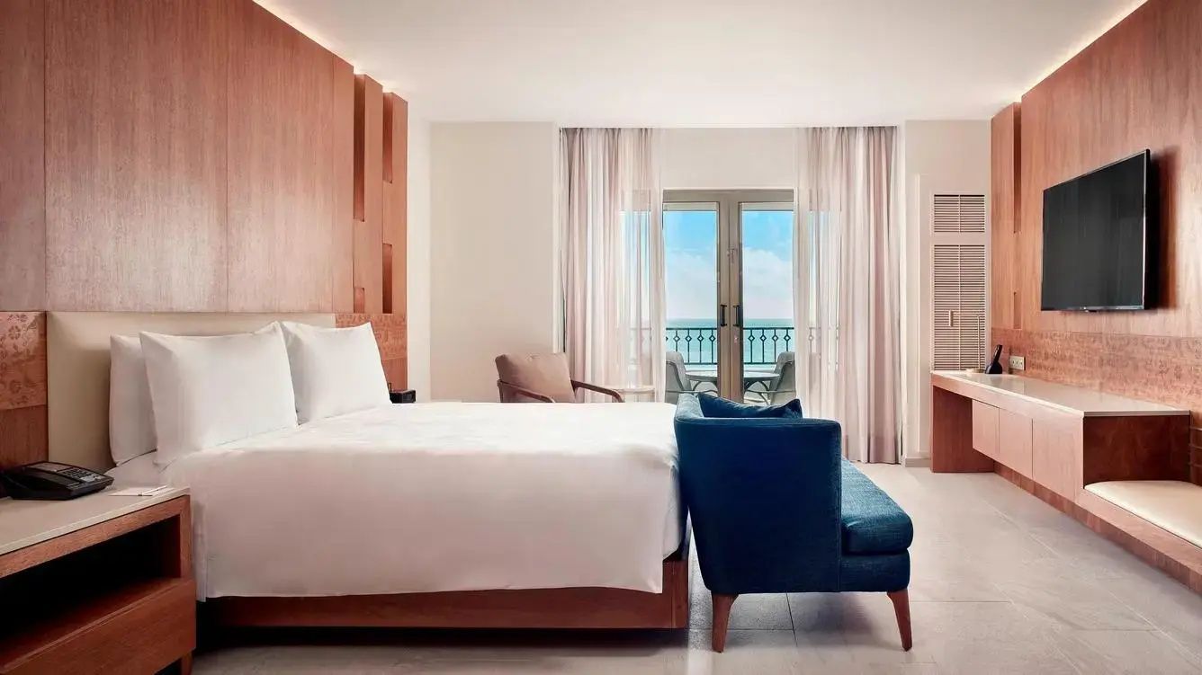 Helles Hotelzimmer mit großem Doppelbett, blauer Sitzbank und Fenster zum Meer.