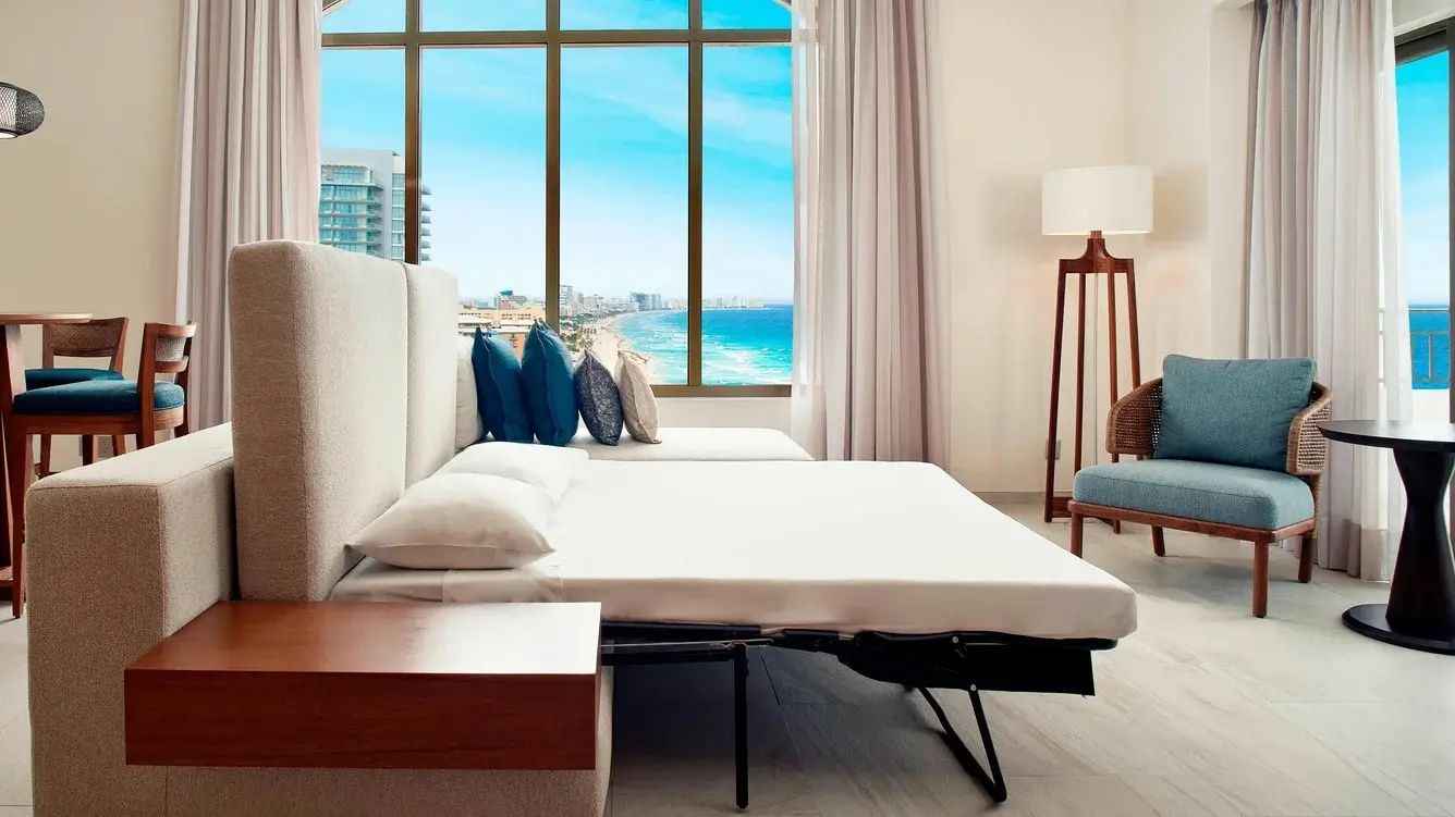 Ausgeklapptes Schlafsofa in einem Hotelzimmer mit Blick auf die Küste und das Meer.