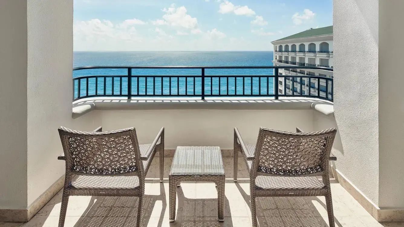 Balkon mit zwei geflochtenen Stühlen und Beistelltisch mit Aussicht auf das meeresblaue Wasser.