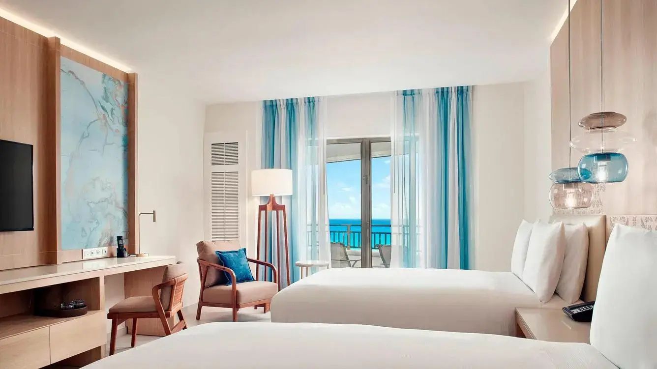 Zweibettzimmer mit hellen Möbeln, blau gestreiften Vorhängen und Balkon zum Meer.
