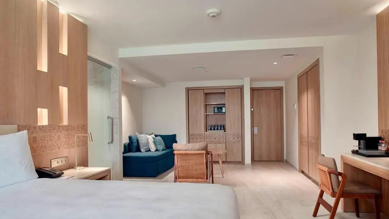 Wohnbereich eines Hotelzimmers mit blauem Sofa, Sessel, Holzschränken und Eingangstür.
