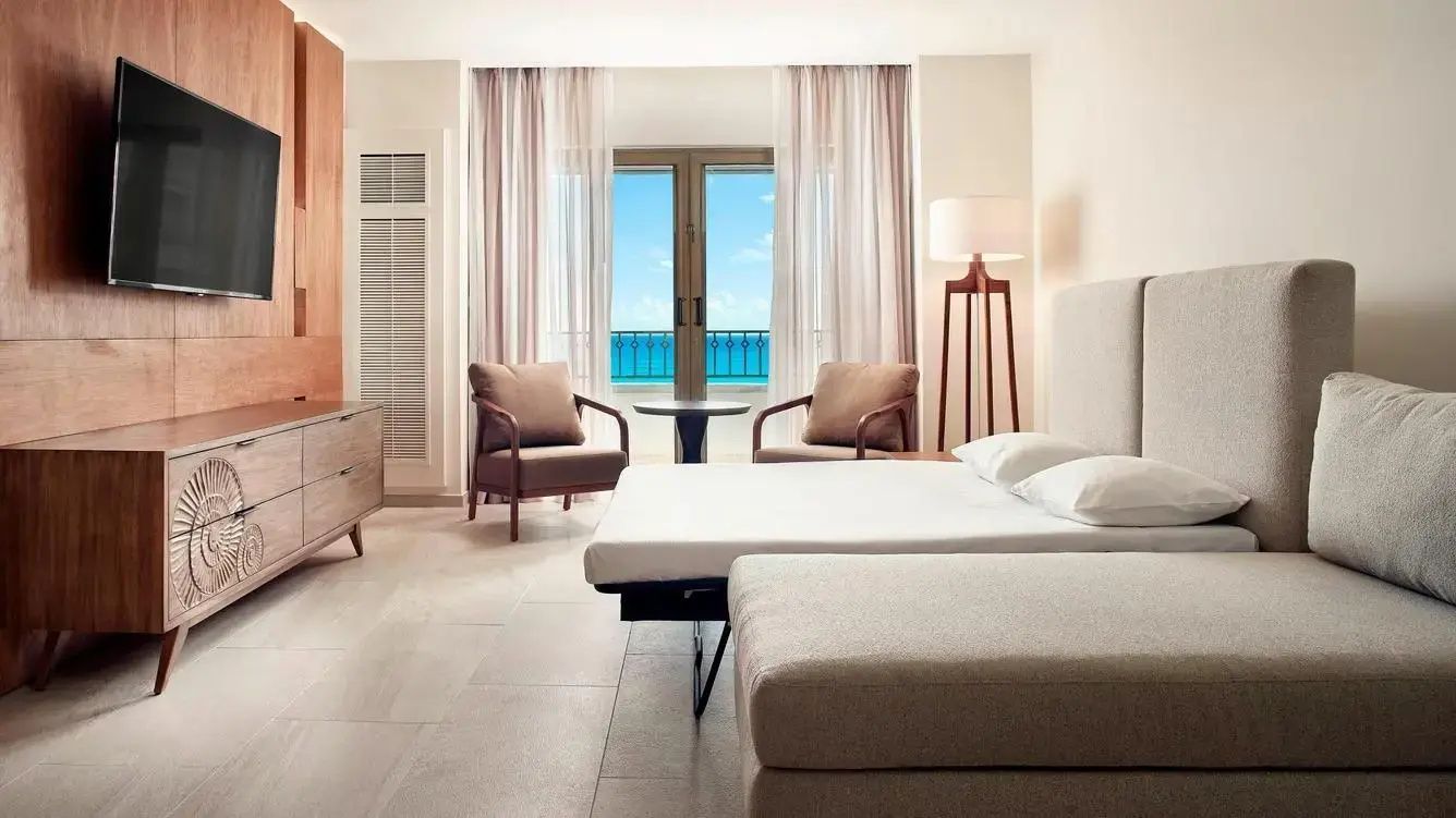 Hotelzimmer mit vorbereitetem Schlafsofa, Sesseln und Blick durch die Balkontür auf das Meer.