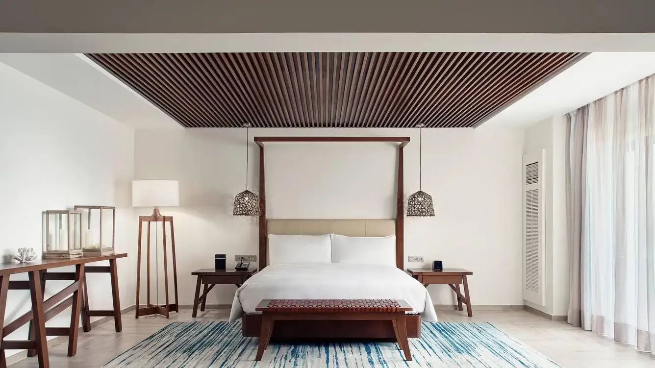 Doppelbett mit Holzkopfteil, Nachttischen und blau gemustertem Teppich im Hotelzimmer.
