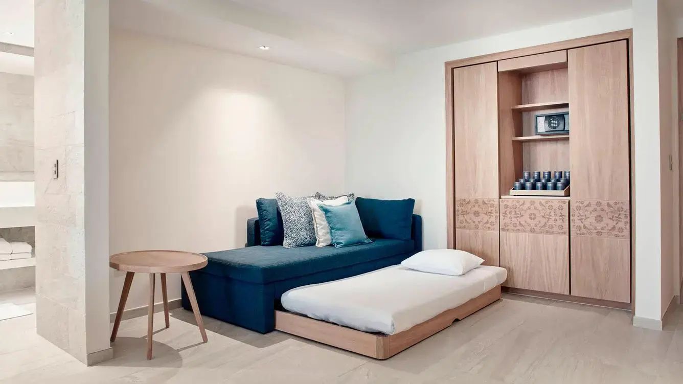 Blaues Schlafsofa mit ausgezogenem Zusatzbett und kleinem runden Holztisch im Zimmer.