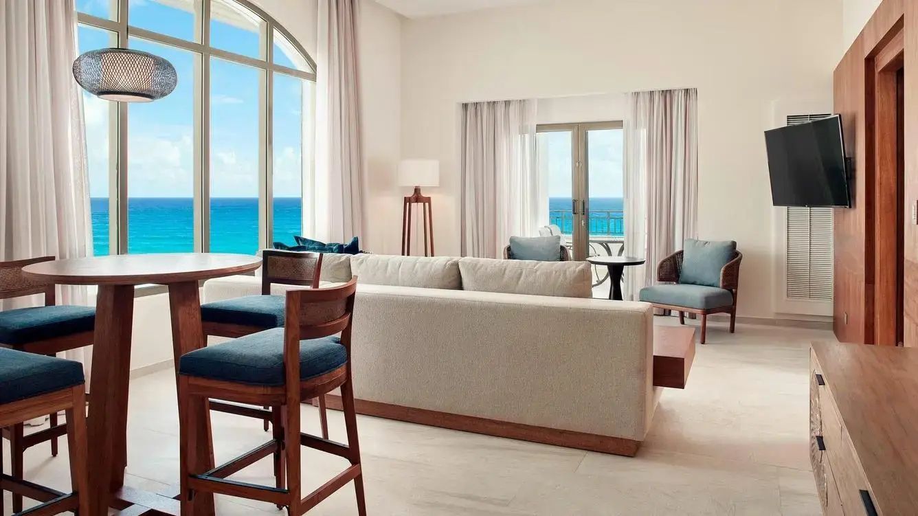 Wohnbereich einer Suite mit hellem Sofa, Sesseln und Fenster mit Blick auf den Ozean.