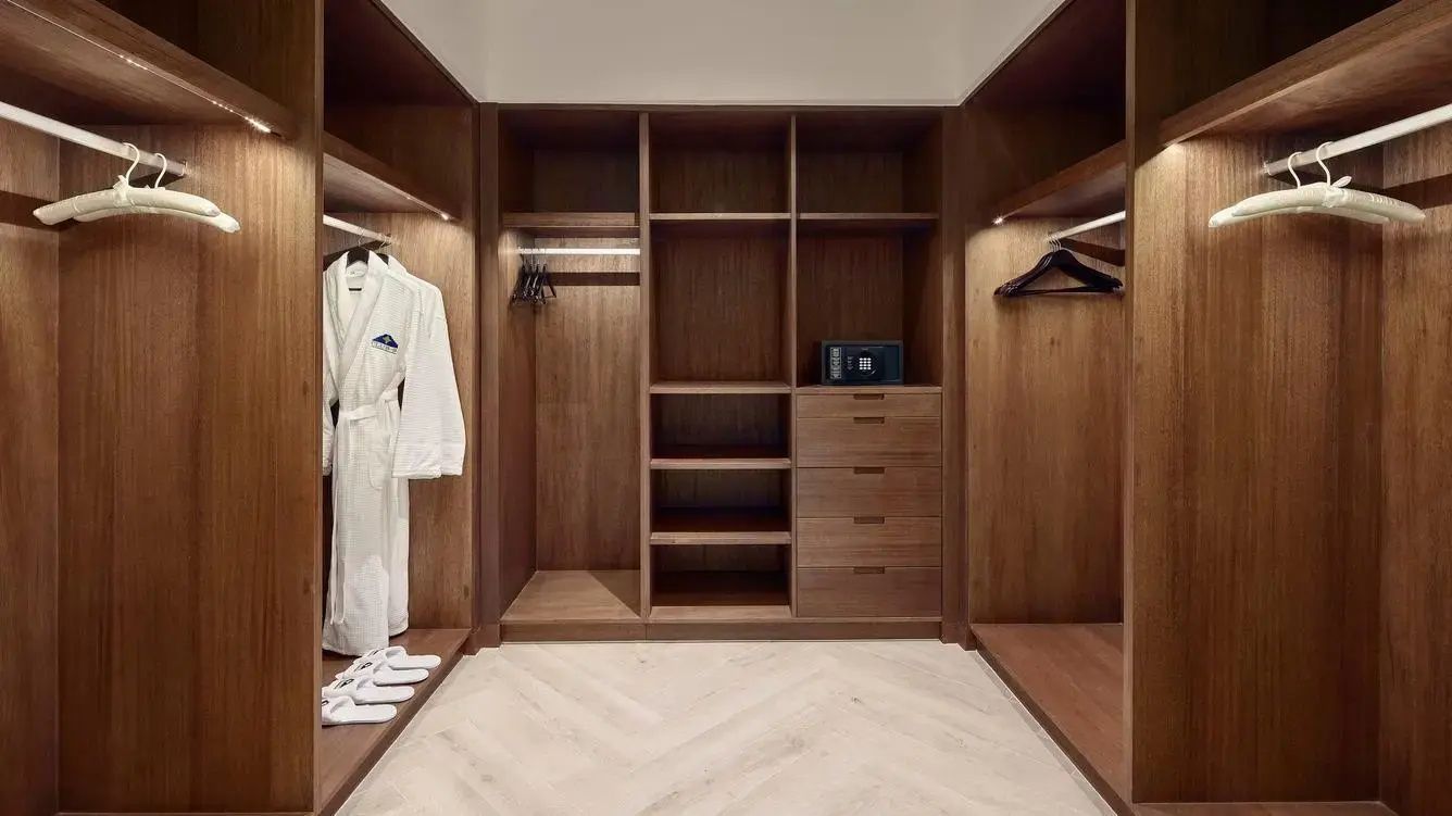 Begehbarer Kleiderschrank aus Holz mit Ablagefächern, Tresor und aufgehängtem Bademantel.
