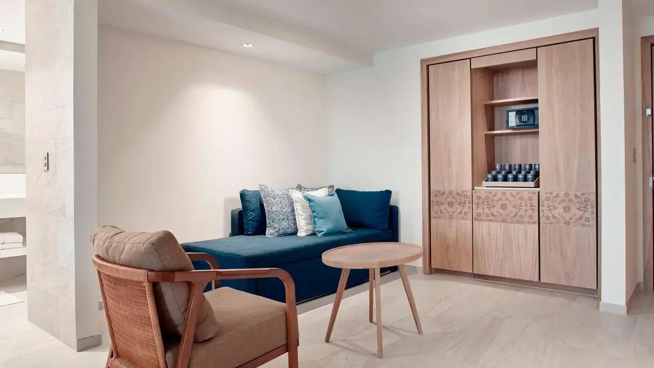 Sitzbereich im Zimmer mit blauem Sofa, Kissen, Holzstuhl und einem runden Beistelltisch.