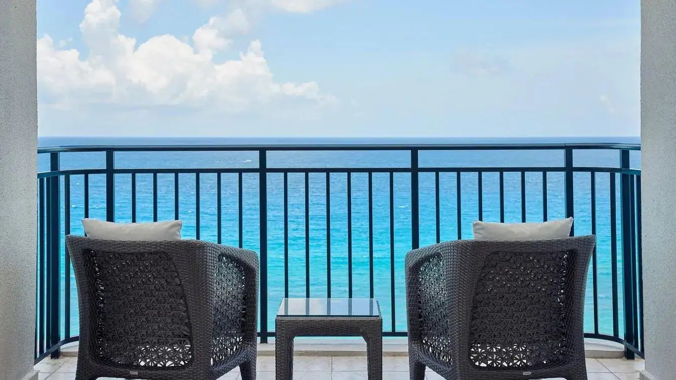 Balkon mit zwei dunklen Flechtsesseln und Blick auf das türkisblaue Meer unter blauem Himmel.