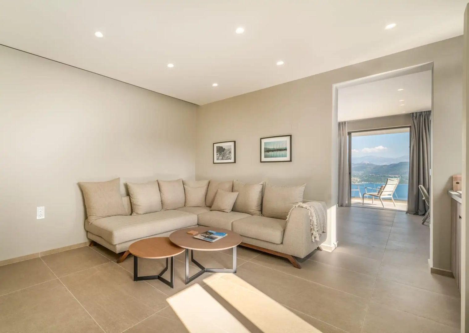Modernes Wohnzimmer mit großer beiger Eckcouch, Couchtischen und Durchgang zum Balkon.