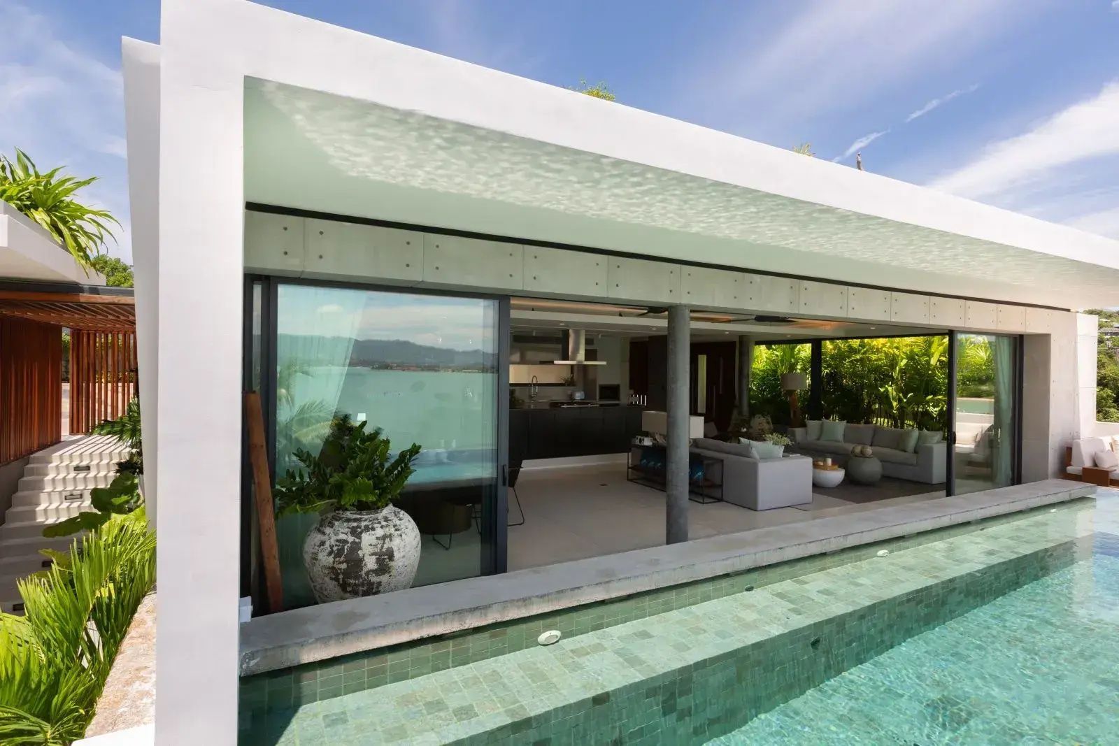 Moderne Villa mit offenem Wohnbereich und direkt angrenzendem Swimmingpool bei Sonnenschein.