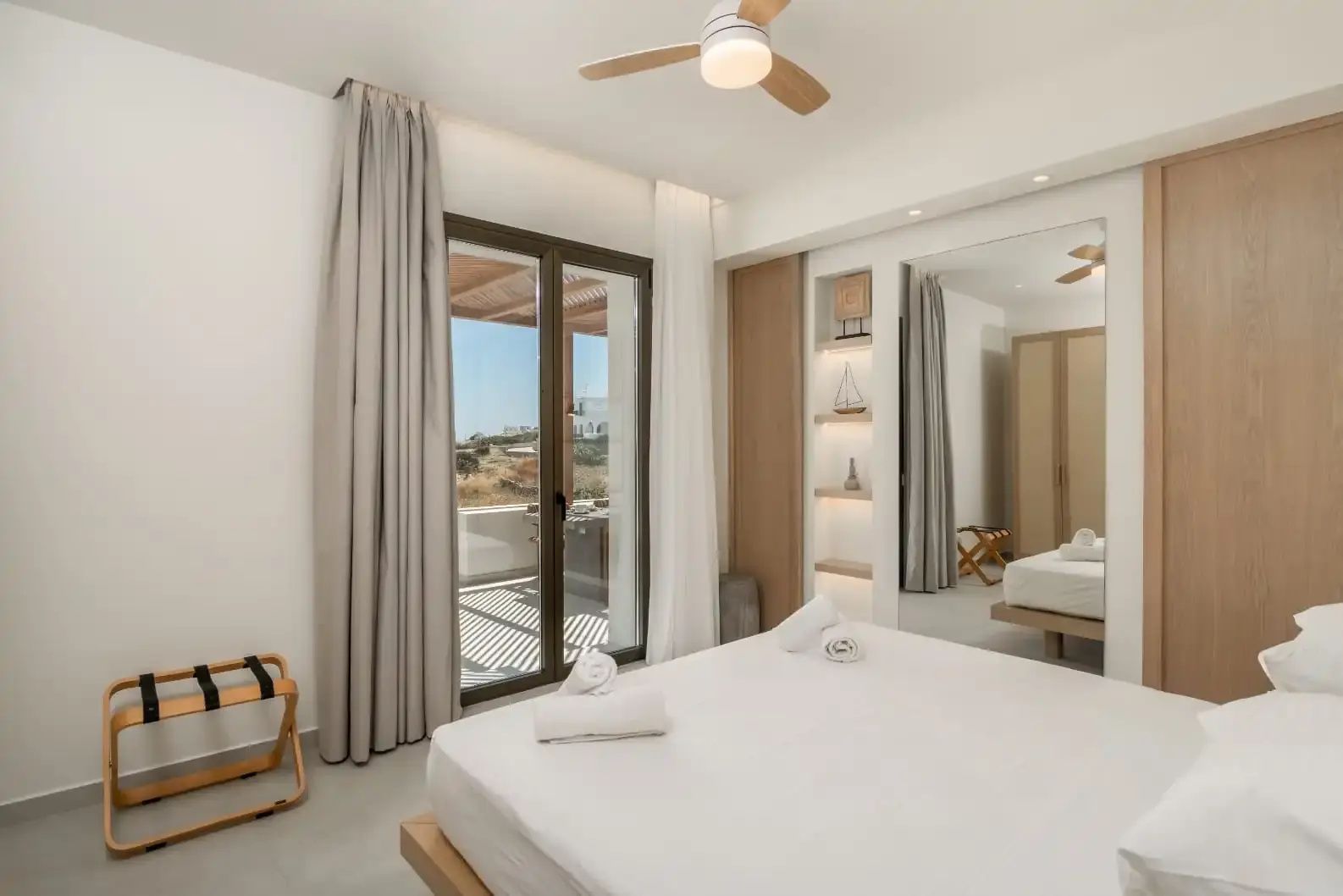 Doppelbett in einem hellen Schlafzimmer mit Deckenventilator und Zugang zur Terrasse.