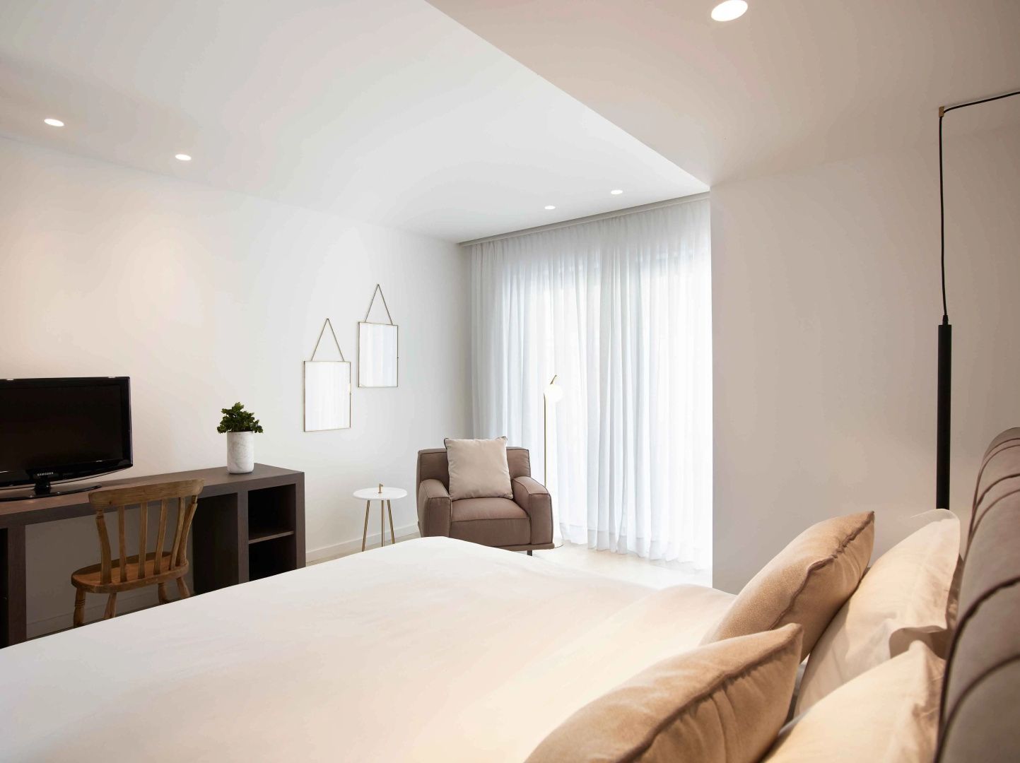 Helles Hotelzimmer mit Sessel, Schreibtisch und großer Fensterfront hinter Vorhängen.